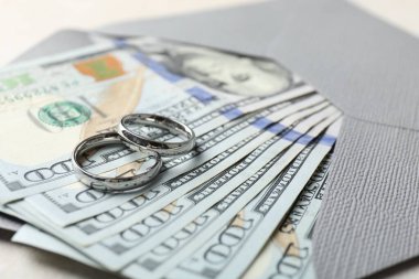 İki gümüş alyans, bir dolarlık banknotlar ve beyaz masanın üzerindeki zarf, yakın plan.