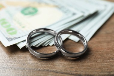 Gümüş alyanslar ve dolar banknotları ahşap masada, yakın plan.