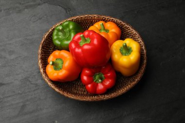 Hasır sepetin içinde taze renkli dolmalık biberler siyah desenli masa, üst manzara.