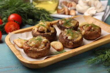 Eritilmiş peynirli, sarımsaklı ve dereotlu leziz mantarlar açık mavi ahşap masada, yakın plan.