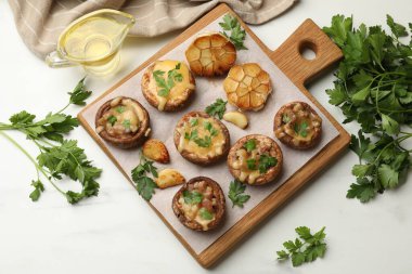 Eritilmiş peynirli, sarımsaklı ve maydanozlu lezzetli mantarlar beyaz masada, düz yerde.