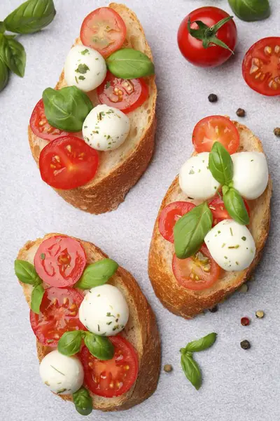 Peynirli, peynirli, domatesli ve fesleğenli lezzetli sandviçler açık gri masada.