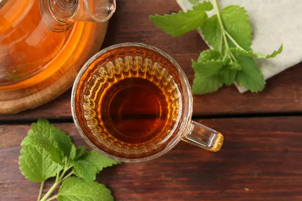Cam bardakta Aromatik limon merhemi çayı, çaydanlık ve taze yapraklar ahşap masada, düz yerde.