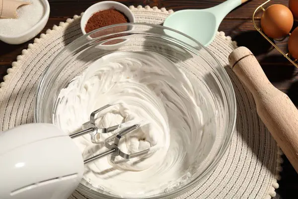 Masanın üstünde çırpılmış krema, yumurta ve diğer ürünlerle el çırpıcı var.