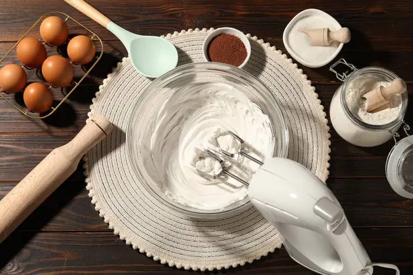 Krem şantili el çırpıcı, yumurta ve diğer ürünler ahşap masada, düz konum