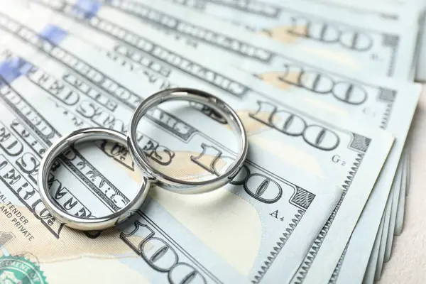 İki gümüş alyans ve bir dolarlık banknotlar beyaz masada, yakın plan.