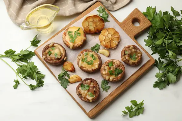 Eritilmiş peynirli, sarımsaklı ve maydanozlu lezzetli mantarlar beyaz masada, düz yerde.