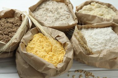 Beyaz ahşap masadaki kağıt torbalarda farklı türde un, yakın plan.