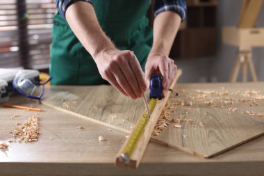 İçerideki ahşap masada bant ile kalas ölçen adam, yakın plan.