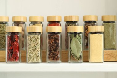 Beyaz masadaki kavanozlardaki farklı aromatik baharatlar, yakın plan.