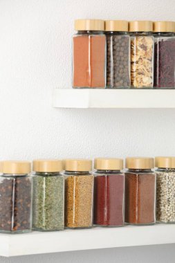 Beyaz raflardaki kavanozlardaki farklı aromatik baharatlar.