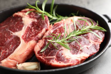 Gri masadaki pişirme kabında çiğ et ve baharat parçaları, yakın plan.