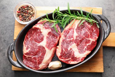 Gri masadaki fırında pişirme kabında çiğ et ve baharat parçaları.