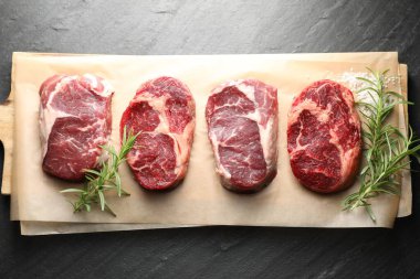 Çiğ et parçaları, biberiye ve tuz siyah masada, üst görünümde.