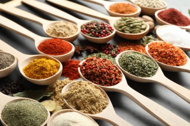 Gri masadaki kaşıklardaki farklı baharatlar, yakın plan.