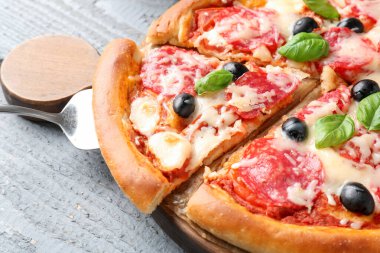 Gri ahşap masada salamlı, peynirli, fesleğenli ve zeytinli lezzetli pizza.