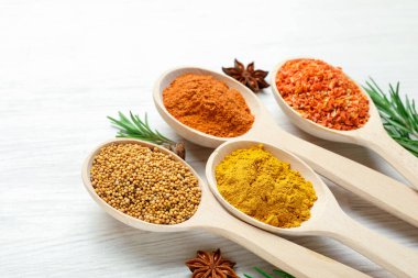 Beyaz ahşap masadaki kaşıklarda farklı aromatik baharatlar, yakın plan.