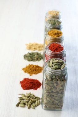 Beyaz masadaki kavanozlarda farklı aromatik baharatlar, yakın plan.