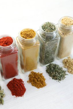 Beyaz masadaki kavanozlarda farklı aromatik baharatlar, yakın plan.