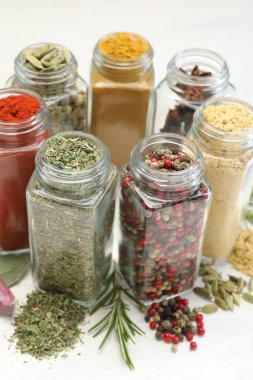 Beyaz masadaki kavanozlarda farklı aromatik baharatlar, yakın plan.