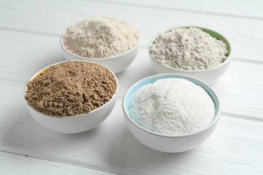 Beyaz ahşap masadaki kaselerdeki farklı un türleri, yakın plan.