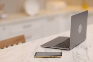 Laptop ve akıllı telefon mutfaktaki beyaz mermer masada, seçici odaklı.