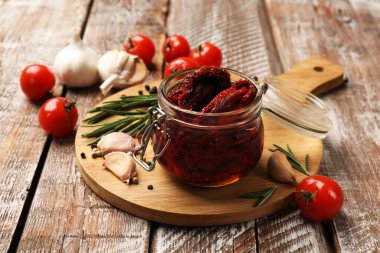 Lezzetli güneşte kurutulmuş domatesler, taze sebzeler, biberiye ve sarımsak ahşap masada, yakın plan.