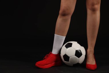 Arka planda futbol topu olan yüksek topuklu ayakkabılı ve spor ayakkabılı bir kadın.