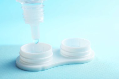 Açık mavi arkaplanda kontak lensleri olan çözelti dosyaya damlıyor, yakın plan