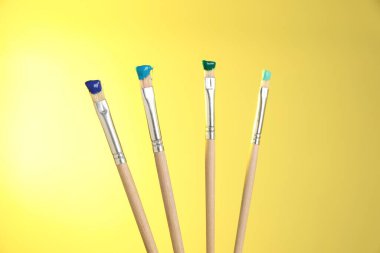 Sarı arkaplanda renk boyalı birçok fırça, yakın plan