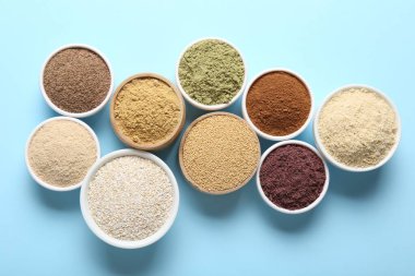 Açık mavi arka planda, kaselerde farklı süper yiyecek tozları var.