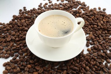 Fincanda Aromatik kahve ve beyaz arka planda fasulye, yakın plan.