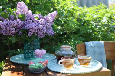 Vazoda güzel leylak çiçekleri, bahçedeki ahşap masada tatlı ve çay.