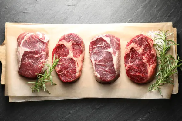 Çiğ et parçaları, biberiye ve tuz siyah masada, üst görünümde.