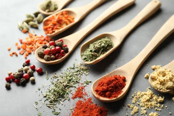 Gri masadaki kaşıklardaki farklı baharatlar, yakın plan.