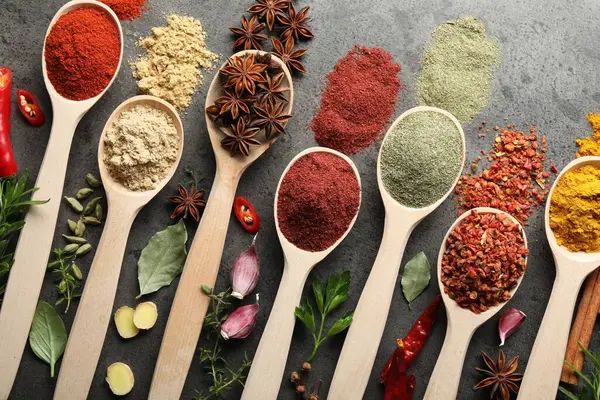 Gri masadaki kaşıklardaki farklı baharatlar düzdü.