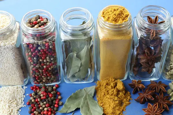 Mavi arka planda kavanozlardaki farklı aromatik baharatlar, yakın plan.