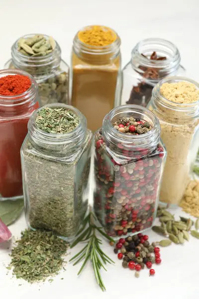 Beyaz masadaki kavanozlarda farklı aromatik baharatlar, yakın plan.
