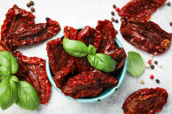 Lezzetli güneş kurutulmuş domatesler kasede ve baharatlar gri masada, düz yatıyordu.