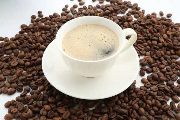 Fincanda Aromatik kahve ve beyaz arka planda fasulye, yakın plan.