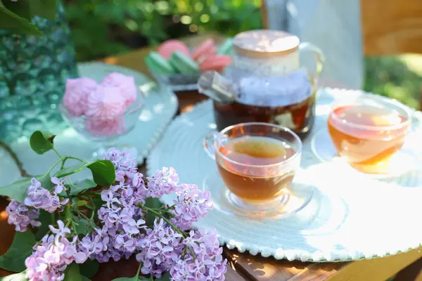 Bahçedeki ahşap masada güzel leylak çiçekleri, tatlılar ve çay, yakın plan.