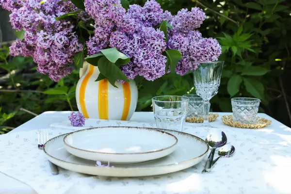 Güzel leylak çiçekleri, tabaklar, çatal bıçaklar, bardaklar ve mumlar bahçede, yakın plan.
