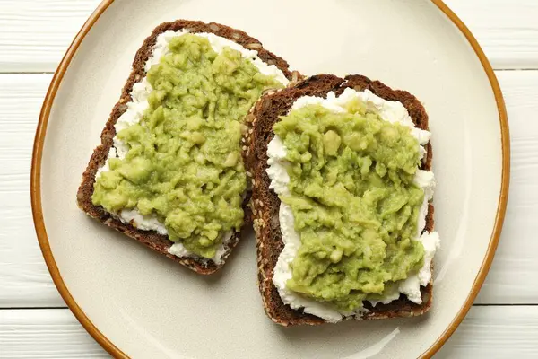 Beyaz ahşap masada avokado ve krem peynirli lezzetli sandviçler.