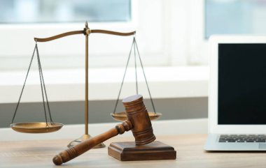 Dizüstü bilgisayar, yargıç tokmağı ve terazileri ofisteki ahşap masada.