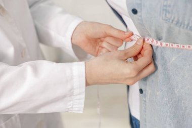 Kilo kaybı. Klinikte kilolu kadının belini bantla ölçen beslenme uzmanı.