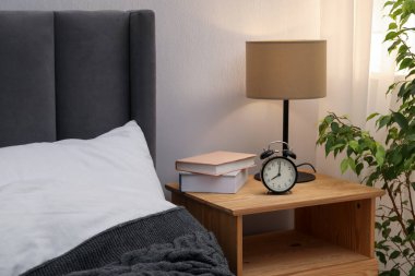 İçinde lamba, çalar saat ve yatağın yanında kitaplar olan komodin. İç tasarım