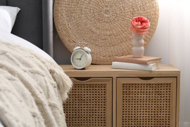 Yatağın yanında çalar saati, dekorasyonu ve kitapları olan bir komodin.