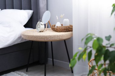 Yan masada ayna, çalar saat ve yatağın yanında dekor var.