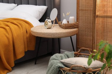 Yan masada ayna, çalar saat ve yatağın yanında dekor var.