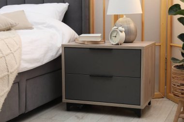 İçinde lamba, çalar saat ve yatağın yanında kitaplar olan komodin.